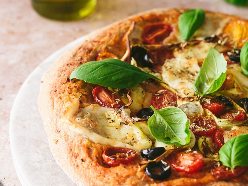 imagem de pizza caseira com queijo mozarella, azeitonas, tomate cereja e folhas de manjericão